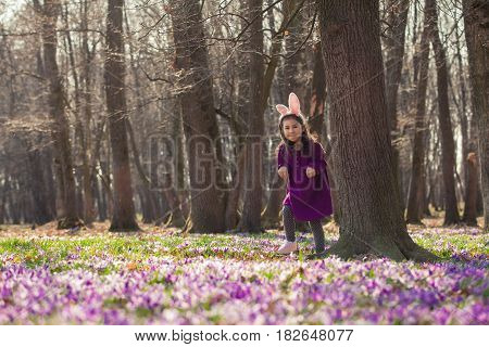 Little girl with banny ears peeping from behind a tree in the park