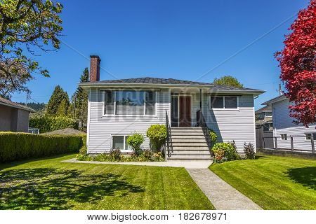 Old modest residential house with concrete pathway over front yard lawn. Family house with freshly mowed lawn on sunny day