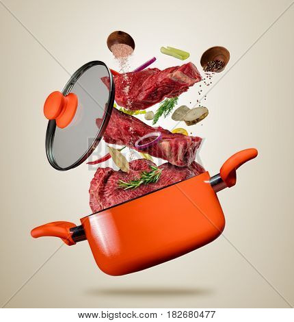 Fresh beef meat pieces with vegetable and cooking ingredients flying into a pot with lit, separated on gray background