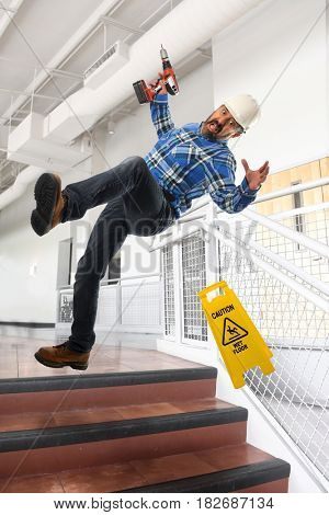 Worker wearing hard hat falling down on stairs inside building
