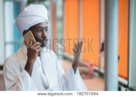Sudanese business man in traditional outfit using mobile phone in office.