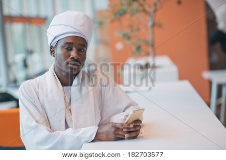 Sudanese business man in traditional outfit using mobile phone in office.