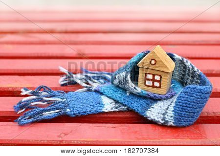Small wooden house with window in a warm blue scarf on the red surface / real estate insurance