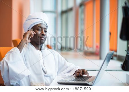 Sudanese business man in traditional outfit using mobile phone in office.