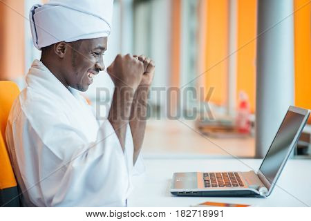 Sudanese business man in traditional outfit using mobile phone in office.