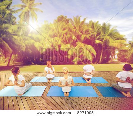 fitness, yoga, meditation and sport concept - group of people exercising in reverse prayer pose over natural background with palm trees 