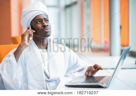Sudanese business man in traditional outfit using mobile phone in office.