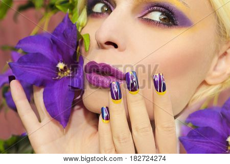Lilac summer makeup and manicure with a design on the nails on the woman with the clematis closeup.Nail art.