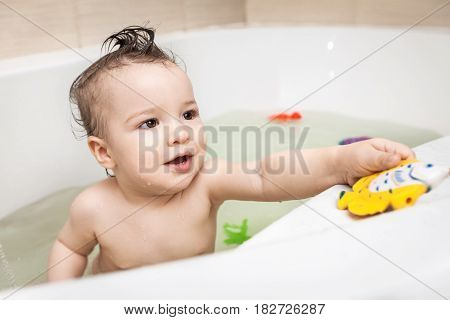 Cute happy little child with strange hairdo taking bath with color toys. Cpncept of child's hygiene, healthy lifestyle, carefree childhood