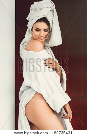 sexy young girl with dark hair, big eyes and dark eyebrows wearing white bath robe whith towel on her head. Model with light nude make-up, white studio background, beauty photo