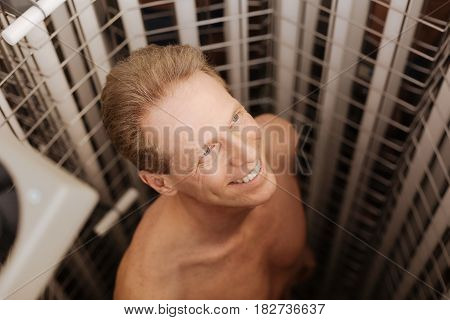 Getting perfect cosmetic tan. Cheerful positive athletic man enjoying wellness procedure in the beauty salon and standing in the tanning both while smiling