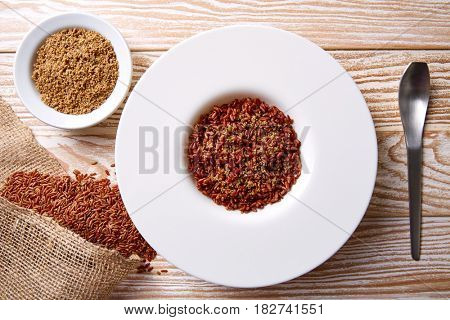 Red wild rice with sesame gomasio seasoning in a white plate over wooden board