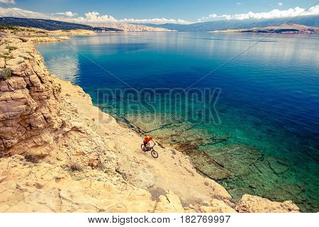 Mountain biker riding on bike in summer inspirational mountains and sea landscape. Man cycling MTB on enduro trail track at seaside and rocky dirt path. Sport fitness motivation and inspiration.