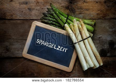 Green and white asparagus and a blackboard with german text Spargelzeit that means asparagus time on a rustic wooden background top view from above copy space selective focus