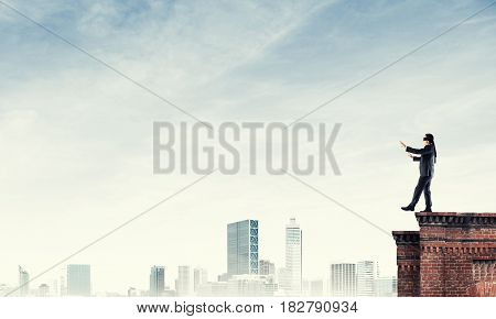 Businessman with blindfolder on eyes walking on building top