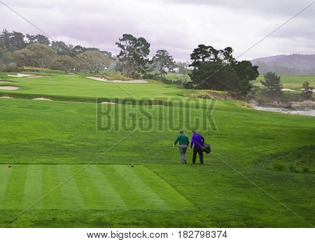 Golfer and caddie walk down fairway after teeing off