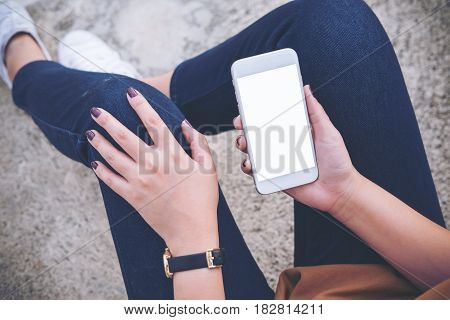 Mockup image of a woman sitting on the street and holding mobile phone with blank white screen