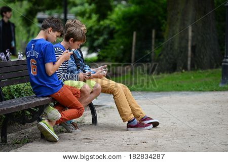 RIGA LATVIA - JULY 27 2016: Unknown young company sitting on a park bench and in smartphone play Pokemon Go.
