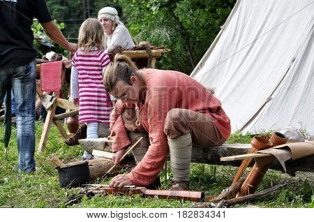 TERVETE LATVIA - AUGUST 13 2011: Historical Zemgalu days. Unknown man in ancient dress sits on a bench and repairing ancient weapons.
