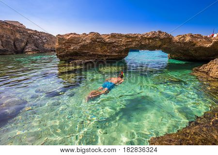 Blue Lagoon Malta - Snorkeling tourist at the caves of the Blue Lagoon on the island of Comino on a bright sunny summer day with blue sky
