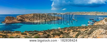 Comino Malta - Panoramic skyline view of the famous and beautiful Blue Lagoon on the island of Comino with sailboats traditional Luzzu boats and tourists enjoying the azure mediterranean sea water and sunshine