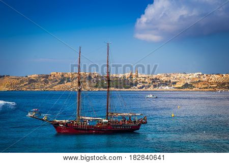 Blue Lagoon Malta - Old sailing boat at the Island of Comino next to the famous Blue Lagoon with the Island of Gozo and town of Mgarr at the background on a sunny summer day