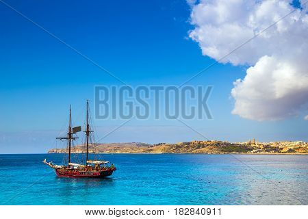 Blue Lagoon Malta - Old sailing boat at the Island of Comino next to the famous Blue Lagoon with the Island of Gozo and town of Mgarr at the background on a sunny summer day