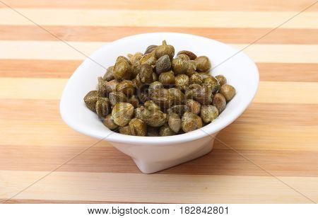 bowl with fresh capers on wooden table.