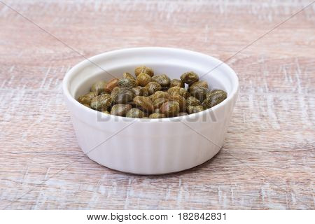 bowl with fresh capers on wooden table.