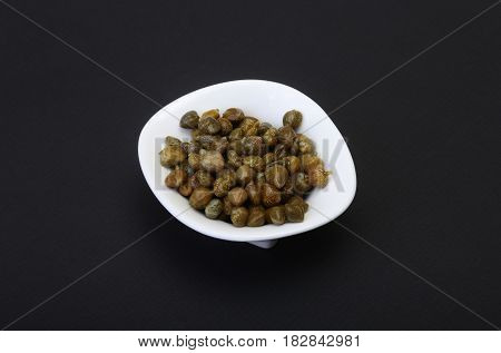 bowl with fresh capers isolated on black background