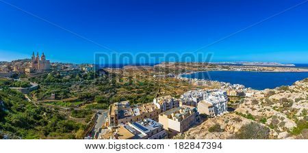 Il-Mellieha Malta - Beautiful panoramic skyline view of Mellieha beach and Mellieha town on a bright summer day with Paris Church Agatha Red Tower and island of Gozo at background with clear blue sky