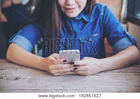 A woman holding and using smart phone on wooden table with feeling relax and smiley face while sitting in vintage cafe