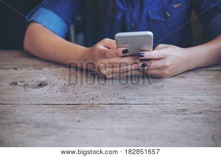A woman holding and using smart phone on wooden table with feeling relax while sitting in vintage cafe
