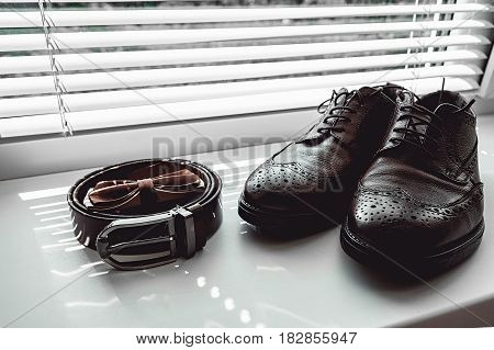 Brown bow tie, leather shoes and belt. Grooms wedding morning. Close up of modern man accessories on the window sills with shutters. Look from above