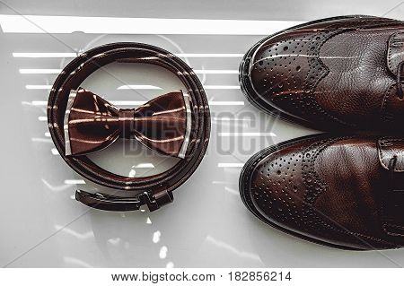 Brown bow tie, leather shoes and belt. Grooms wedding morning. Close up of modern man accessories on the window sills with shutters. Look from above