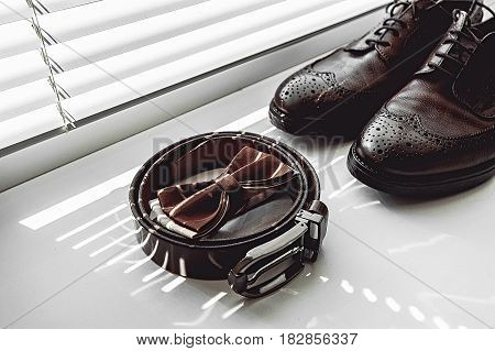 Brown bow tie, leather shoes and belt. Grooms wedding morning. Close up of modern man accessories on the window sills with shutters. Look from above
