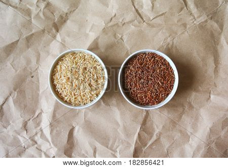 Two bowls of brown and red uncooked rice on rough paper background.