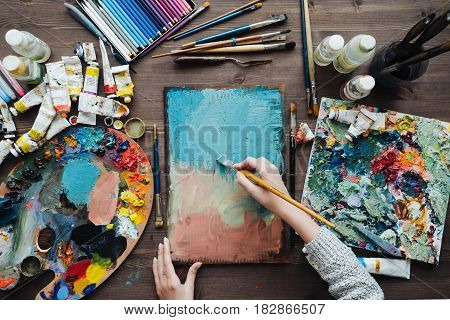 Painter workplace top view photo. Artist paintbrushes colorful paints and crayons assorted on the desk.