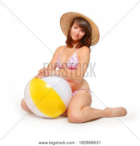Overweight woman dressed in bikini and straw hat exercising with ball and preparing for summer holidays on the beach.
