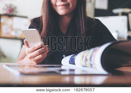 A beautiful Asian woman using smart phone while reading book in the bistro cafe with smiley face
