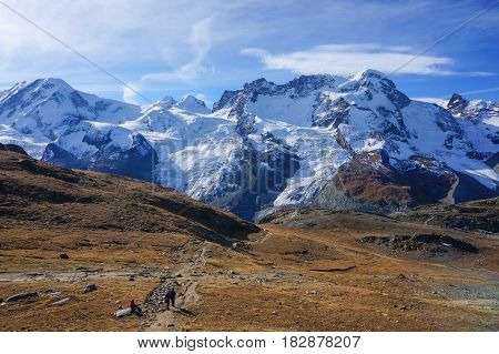 View of people hiking on red cold stone rock mountain with the background of snow alps in autumn