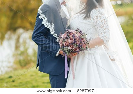 the bride and groom on your wedding day for a walk holding wedding bouquet. The groom and the bride covered by a veil