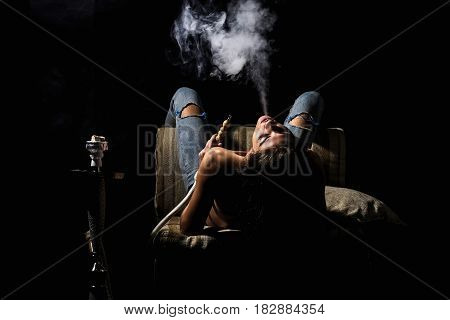 naked girl smoking hookah pretty woman with sexy back and body in jeans sitting on eastern chair with shisha bong or kalian as arabic tradition on black background