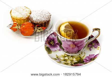 Mug of tea with lemon and and two cupcakes on isolated white background
