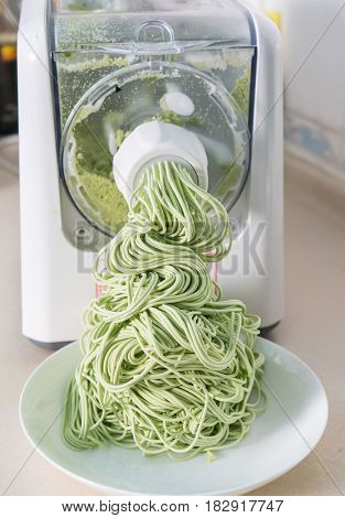 Green spaghetti pasta sheet being processed in machine 