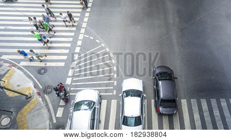 people walk on across the pedestrian crosswalk street with the transportation cars and motorcycle go pass the crosswalk junction in the city (Aerial top view)