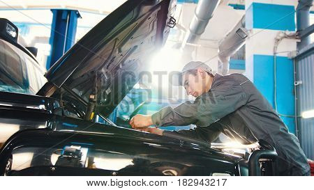 Mechanic in car service - repairing in engine compartment for luxury SUV, wide angle