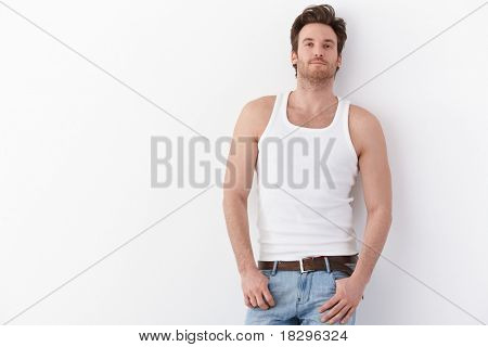 Sexy joven permanente por pared en camiseta, sonriendo.