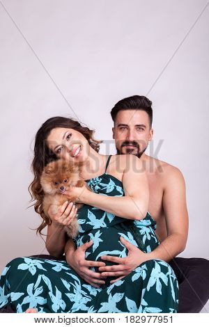 Happu pregnant woman with her husband and dog in studio photo. Wife and husband. Parenthood and expecting baby