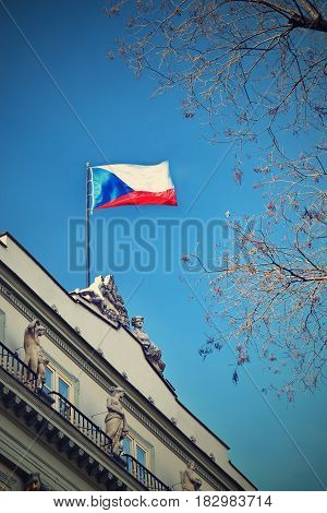 The flag of the Czech Republic on a building with blue sky and the sun in the background.